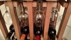 two wine glasses and three bottles in a wooden holder with corks on the bottom