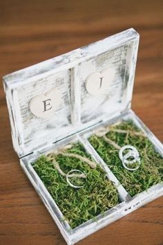 an open box with two rings in it on a wooden table next to some moss