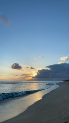 the sun is setting over the ocean with clouds in the sky and sand on the beach