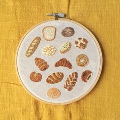 an embroidery project with different types of breads and pastries on the hoop, sitting on a yellow surface