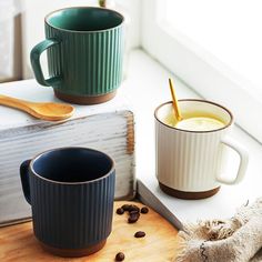 two coffee mugs sitting on top of a table next to a book and spoon