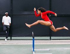 a woman in a red bodysuit jumping over a hurdle