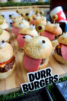 mini burgers with cheese, meat and olives are displayed on a cutting board