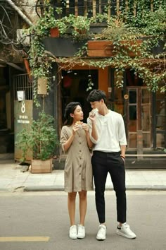 a man and woman standing next to each other in front of a building with ivy growing on it