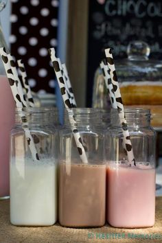 three jars with straws in them sitting on a table next to milk and cookies