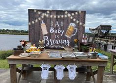 a baby is brewing sign and some food on a picnic table with lights strung over it