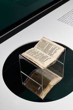 an open book sitting on top of a glass table next to a black plate with papers in it