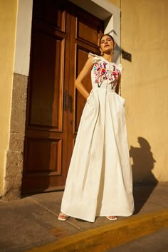 a woman standing in front of a door wearing a white dress and hat with flowers on it