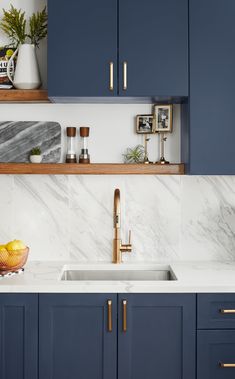 a kitchen with blue cabinets and marble counter tops, gold faucet, brass accents