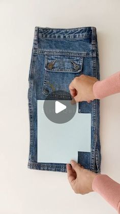 two hands holding a piece of paper in front of a pair of jeans