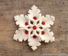 a snowflake made out of felt sitting on top of a wooden table with red beads