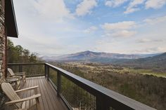 a wooden deck with two chairs on top of it and mountains in the back ground