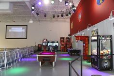 a room filled with lots of arcade machines next to bar stools and neon lights