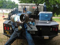 a man sitting on the back of a truck holding a blow dryer up to his face