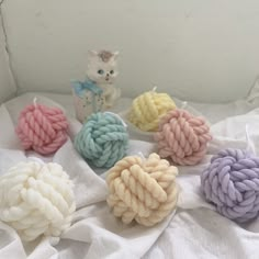 four balls of yarn sitting on top of a white sheet next to a small toy cat