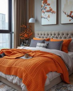 a bed with orange blankets and pillows in a bedroom next to a large glass window