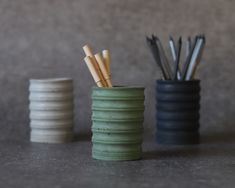 three ceramic cups with toothbrushes in them on a gray surface next to each other