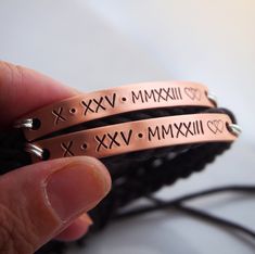 two copper bracelets with roman numerals and hearts are shown in closeup