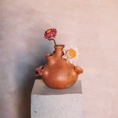 a vase with flowers in it sitting on top of a cement block next to a wall