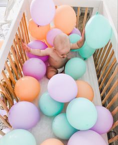 a baby in a crib surrounded by balloons