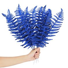 a hand holding a bunch of blue fake plants on a white background in front of a person's hand