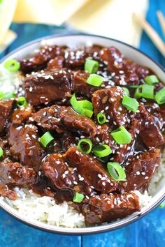 a bowl filled with beef and rice on top of a blue tablecloth next to chopsticks