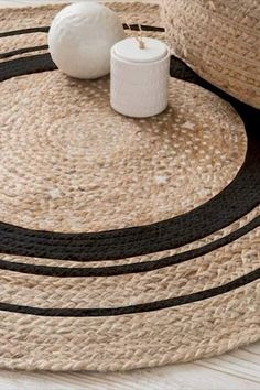 two white candles sitting on top of a black and beige rug next to a straw hat