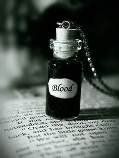 a bottle with blood sitting on top of an open book next to a chain necklace