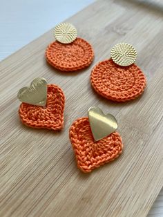 four crocheted heart shaped buttons on a wooden surface with two gold and one orange