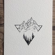 a card with mountains and trees in the middle, on top of a wooden table