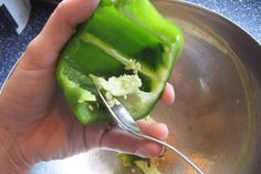 a person holding a spoon in a metal bowl with green peppers on the bottom and inside