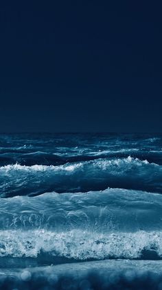 an ocean with waves crashing on the shore and dark blue sky in the back ground