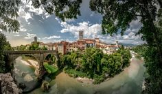 an aerial view of a bridge over a river with buildings on the other side and trees in the foreground