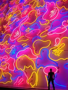 a man standing in front of a neon lit wall with many different shapes and colors