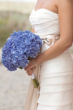 a woman in a white dress holding a bouquet of blue hydrangeas on her wedding day