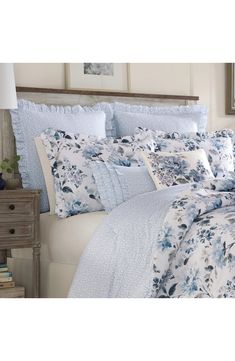 a blue and white comforter set with flowers on it in a bedroom next to a night stand