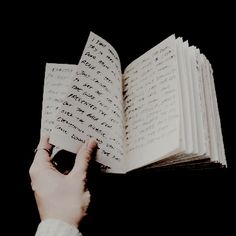 a person is holding an open book in their left hand and touching it with both hands