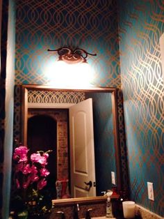 a bathroom sink sitting under a mirror in front of a wallpapered wall with flowers on it