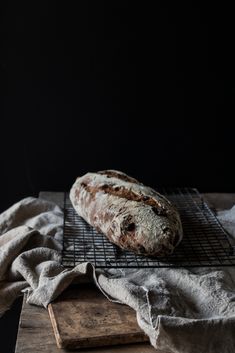 a loaf of bread sitting on top of a cooling rack next to a wooden board