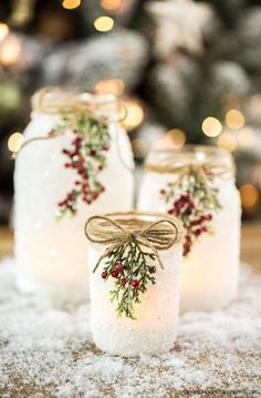 three mason jars decorated with holly and berries are sitting on snow in front of a christmas tree