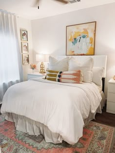 a bed with white sheets and pillows on top of it next to a painting hanging above the bed