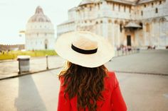 a woman with long hair wearing a white hat in front of a large building,