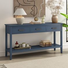 a blue table with some books and vases on it in front of a painting