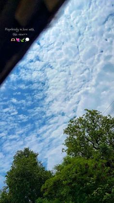 an airplane flying in the blue sky with clouds above it and some trees on either side