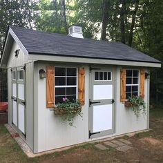 a small shed with windows and shutters on the side, in front of some trees