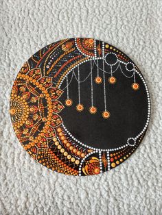 an artistically painted black and orange plate on a white surface with beads hanging from it