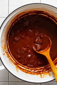 a wooden spoon in a pot filled with brown sauce on top of a tile floor