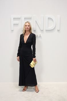 a woman standing in front of a white wall wearing a black dress and holding a yellow purse