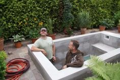 two men sitting in an outdoor hot tub surrounded by greenery and potted plants