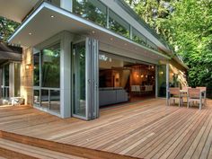 a wooden deck with chairs and tables next to a house in the woods on stilts